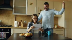 A couple reviews life insurance documents and beneficiary forms together at a kitchen table.
